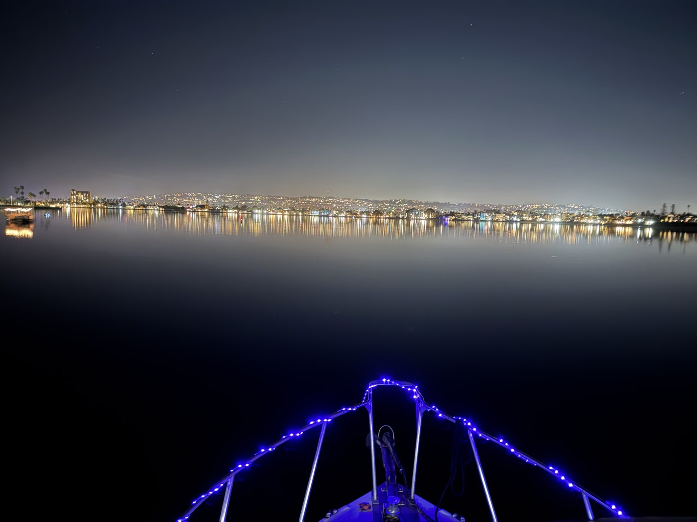 The lit bow rail of the Marissa at night, the bay and city lights ahead
